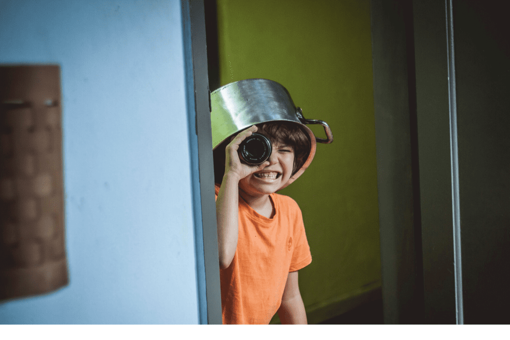 Kid with head on pan looking through lens smiling