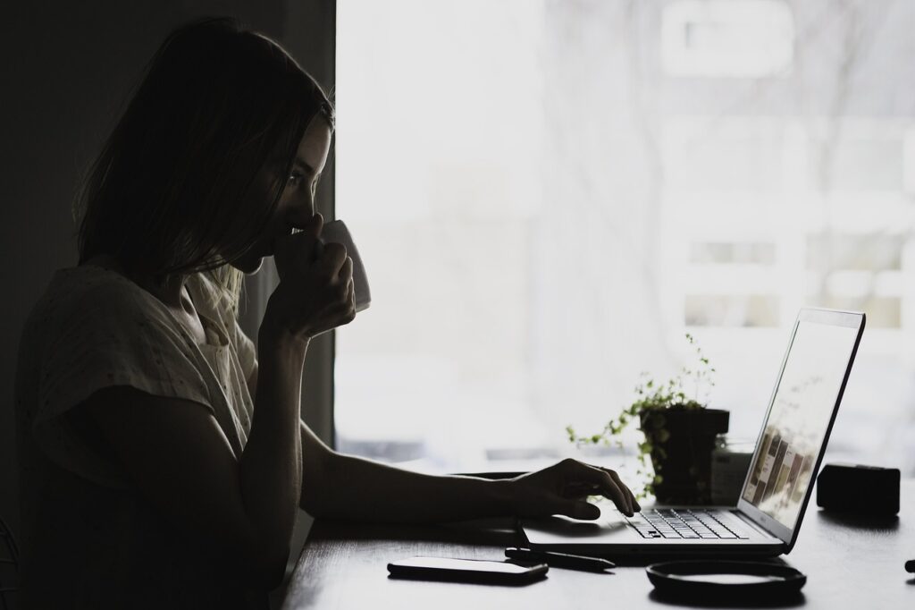 teenage girl sitting in the dark sipping a drink while typing on her computer