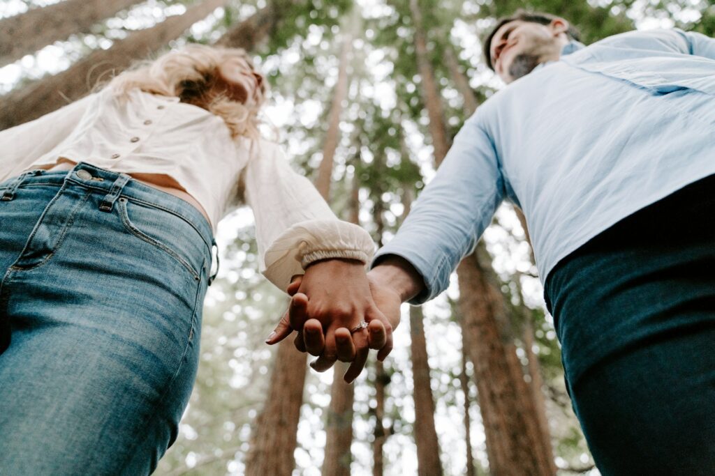 Couple standing side by side holding hands in the fores.