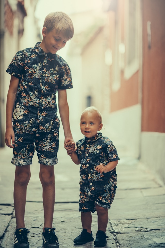 Sibling holding hands with his younger brother, wearing the same clothes looking at him lovingly